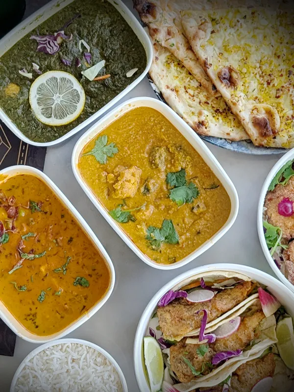 Indian takeaway containers of curry and saag with warm garlic naan and basmati rice, ready to collect.